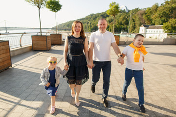 young family dad mom son and daughter are walking the street in the park at sunset and having fun