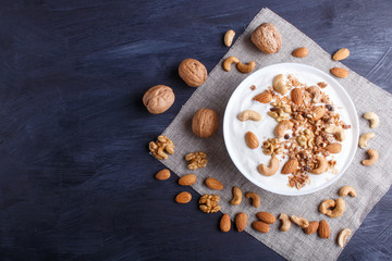 Obraz na płótnie Canvas White plate with greek yogurt, granola, almond, cashew, walnuts on black wooden background.