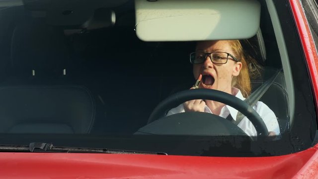 Satisfied business woman makes makeup looking in mirror in sun visor while driving. young businessman traveling to a meeting in the car.
