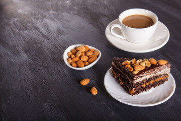 Chocolate cake with caramel, peanuts and almonds on a black wooden background.