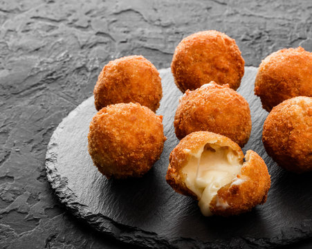 Fried potato cheese balls or croquettes with spices on black plate over dark stone background. Unhealthy food, top view.