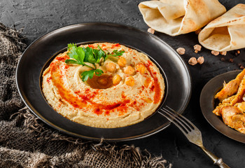 Chickpeas hummus with olive oil, paprika in a plate over dark stone background. Healthy vegan food,...