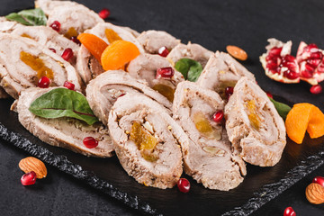 Assorted meat, stuffed chicken roll, meat roll with pomegranate, greens on black shale background. Meat appetizer, food concept. Top view.