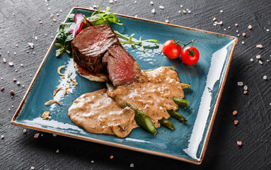 Juicy medium beef fillet steaks mignon with asparagus and mushroom sauce on on dark stone...