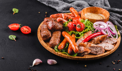 Assorted delicious grilled meat and sausages with tomatoes and bbq sauce on cutting board over black stone background. Hot Meat Dishes, closeup.