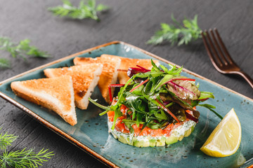 Healthy fresh salad with avocado, salmon, greens, arugula, spinach and cheese with toast in plate over dark background. Healthy vegan food, clean eating, dieting.