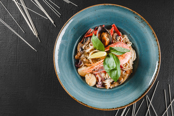 Pasta spaghetti with seafood, langoustine, mussels, oysters, squid in mushrooms sauce on plate over dark stone background. Italian food.