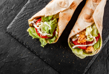 Tortilla wraps with grilled chicken, fresh vegetables and salad on black stone background. Healthy...