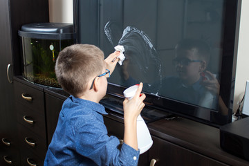 Wycieranie ekranu telewizora z kurzu przez chłopca w wieku szkolnym. 
