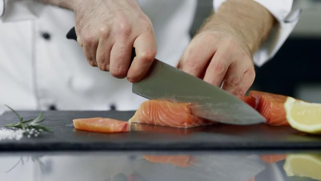 Chef cutting salmon fillet at kitchen. Closeup hands slicing fresh fish.