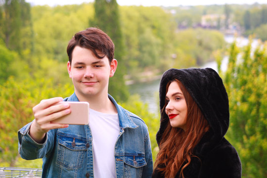 Couple using technology with smartphone. A smiling boy and girl make a selfie in nature. Teenage couple taking pictures of themselves outdoors