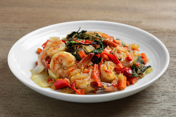 close up of stir fried shrimps with basil in a ceramic dish on wooden table. hot and spicy thai style food menu.