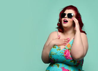 Plus-size lady overweight woman in sunglasses and colorful sundress talks on cell-phone and hear someting breathtaking 