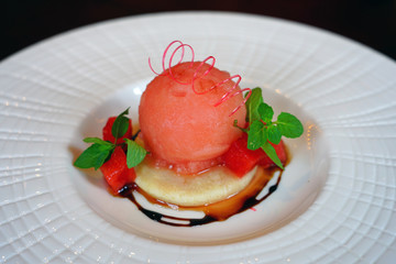 View of a gourmet dessert plate with a scoop of red watermelon sorbet with a sugar twist on top