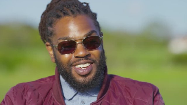Handsome black male with sunglasses and dreadlocks reacts during a conversation 
