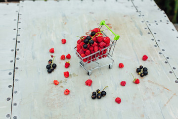 Mini shopping basket full of fresh red ripe raspberry and blackberry on vintage background