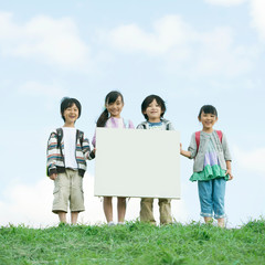 草原でメッセージボードを持ち微笑む小学生