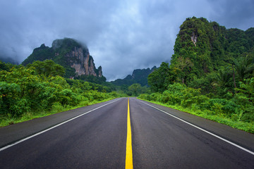 Asphalt road and mountains landscape under fog from rain with clouds