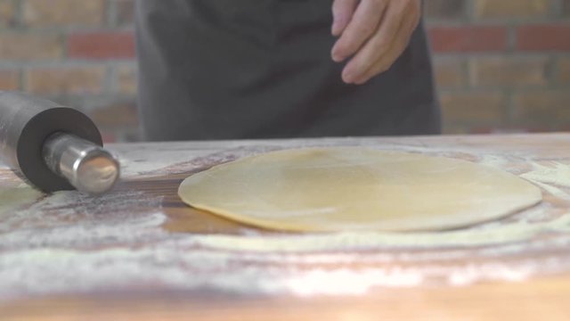 Rolling dough with roller pin for baking pie on kitchen table. Chef hands rolling dough for pizza with roller in pizzeria. Baking pastry and cake in bakery. Married man cooking homemade food.