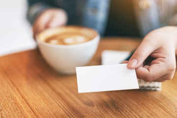 A woman holding and giving a blank empty business card to someone while drinking coffee