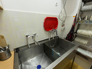 Closeup of a metal sink in the kitchen of the restaurant, pipe, faucet, dishes