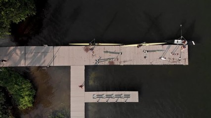 Steady aerial top down view of a rowing landing stage and training facility in the city lake of Rio de Janeiro with rowers arriving and coming out of the water taking the boats to storage out of frame - Powered by Adobe