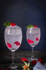 Sparkling cold water detox with rose and ice on the wood table there are rose and same object placed around.