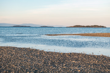 sandy beach filled with tiny rocks at low tide during sunset with islands over the horizon