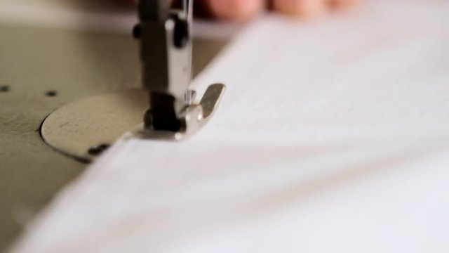 Close up of a sewing machine operated by a tailor. Sewing a white piece of cloth.