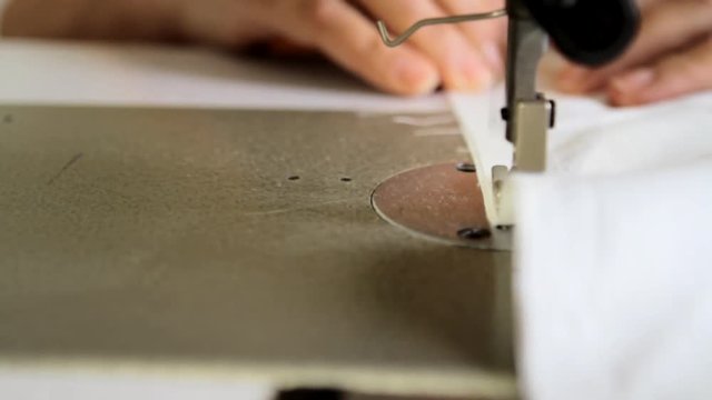 Tracking shot close up of a sewing machine operated by a tailor. Repairing a white piece of cloth.