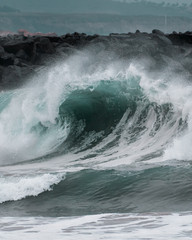 A large barreling wave crashing onto the shore spraying mist