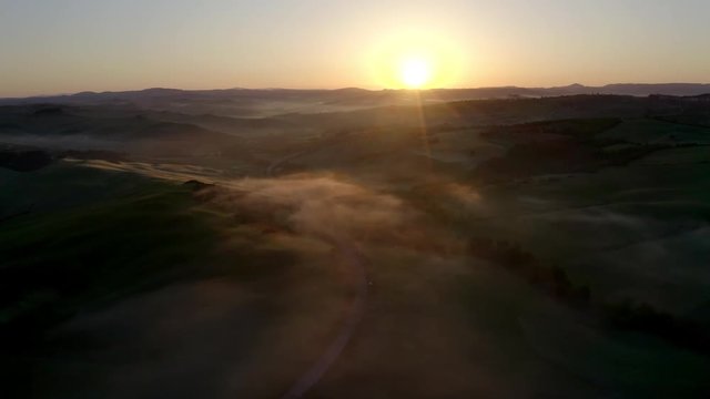 Amazing drone shot at sunrise with morning fog and dew above green cypress hills in Val D'Orcia, Tuscany, Italy. Aerial view of a beautiful landscape at sunrise with mist