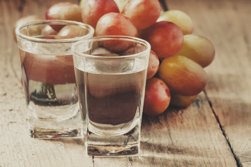 Grappa in small glass and ripe grapes on old wooden table, selective focus