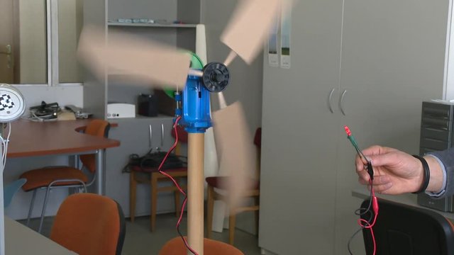 Scientist hand hold burning bulb and wind turbine model rotate in laboratory