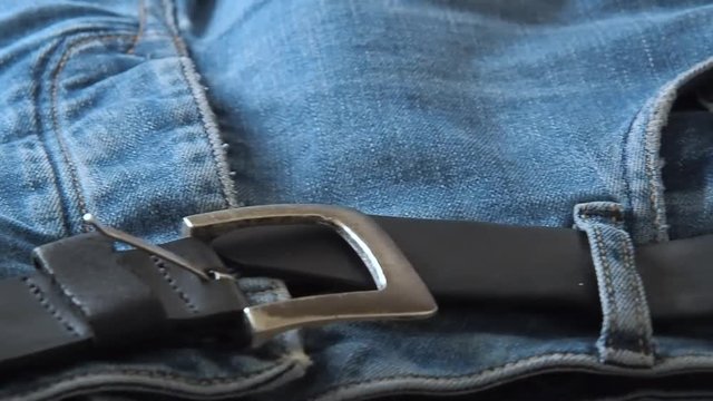 Blue jeans with leather belt laying on table, close shot. Blurred background. Selective soft focus. Camera moving along belt and front trouser pockets. Background for fashion banners and wallpapers