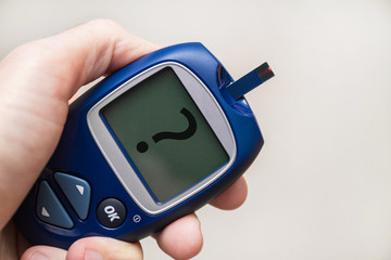 Man holding glucometer with test strip with question mark on the monitor. Blood glucose meter. Closeup, selective focus