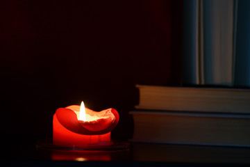 Red burning candle and old books in the dark close up