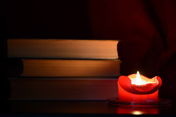 Red burning candle and old books in the dark close up