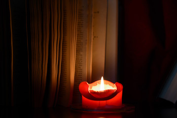 Red burning candle and old books in the dark close up
