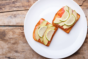 Fresh salmon sandwich with avocado and lime on white plate