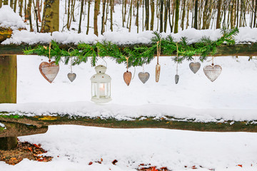 Fir garland, iron lantern and wooden hearts hanging in winter garden.