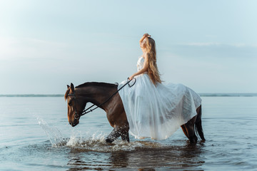 Beautiful girl in a white long dress riding a horse. Bride in the lake on horseback.