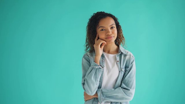 Portrait of pretty African American woman in trendy outfit thinking dreaming on blue background looking at camera and smiling. People and thoughts concept.