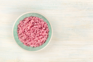 A bowl of pink Himalayan sea salt, shot from the top on a white wooden background with copy space