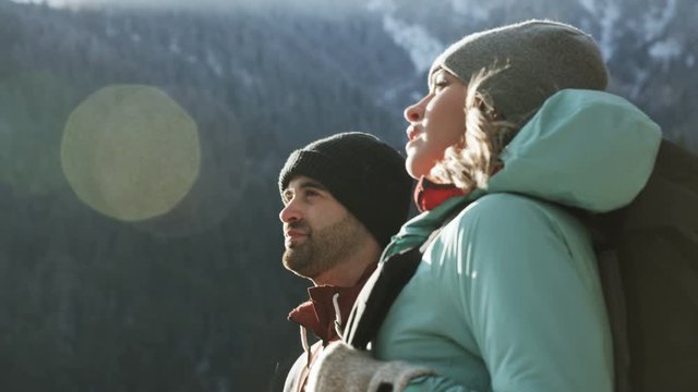 Man and woman walk into frame, stop to take in view of snowy mountains