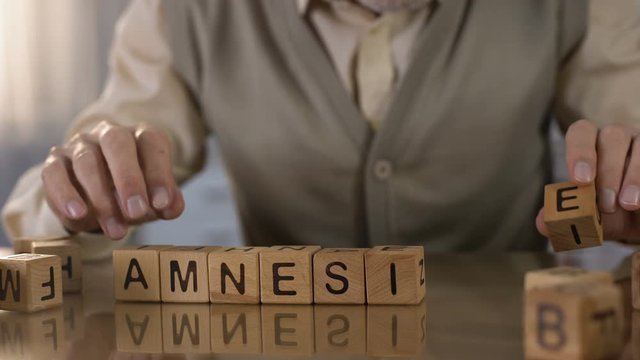 Elderly pensioner making word amnesia of wooden cubes on table, health care