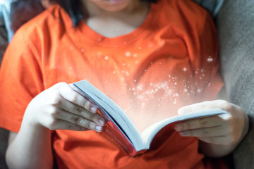 Reading education concept. Asia child girl read a young adult fiction book with sparkle light...