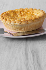 Steak and ale pie cooked on a pink plate with a stainless steel serving utensil on a grey wood background