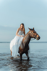 Beautiful girl in a white long dress riding a horse. Bride in the lake on horseback.