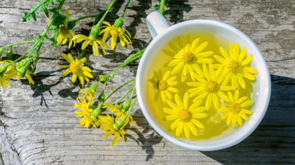 Closeup of a cup of tea on a wooden table. Nearby are flowers. Still life with a cup of tea. Top view.